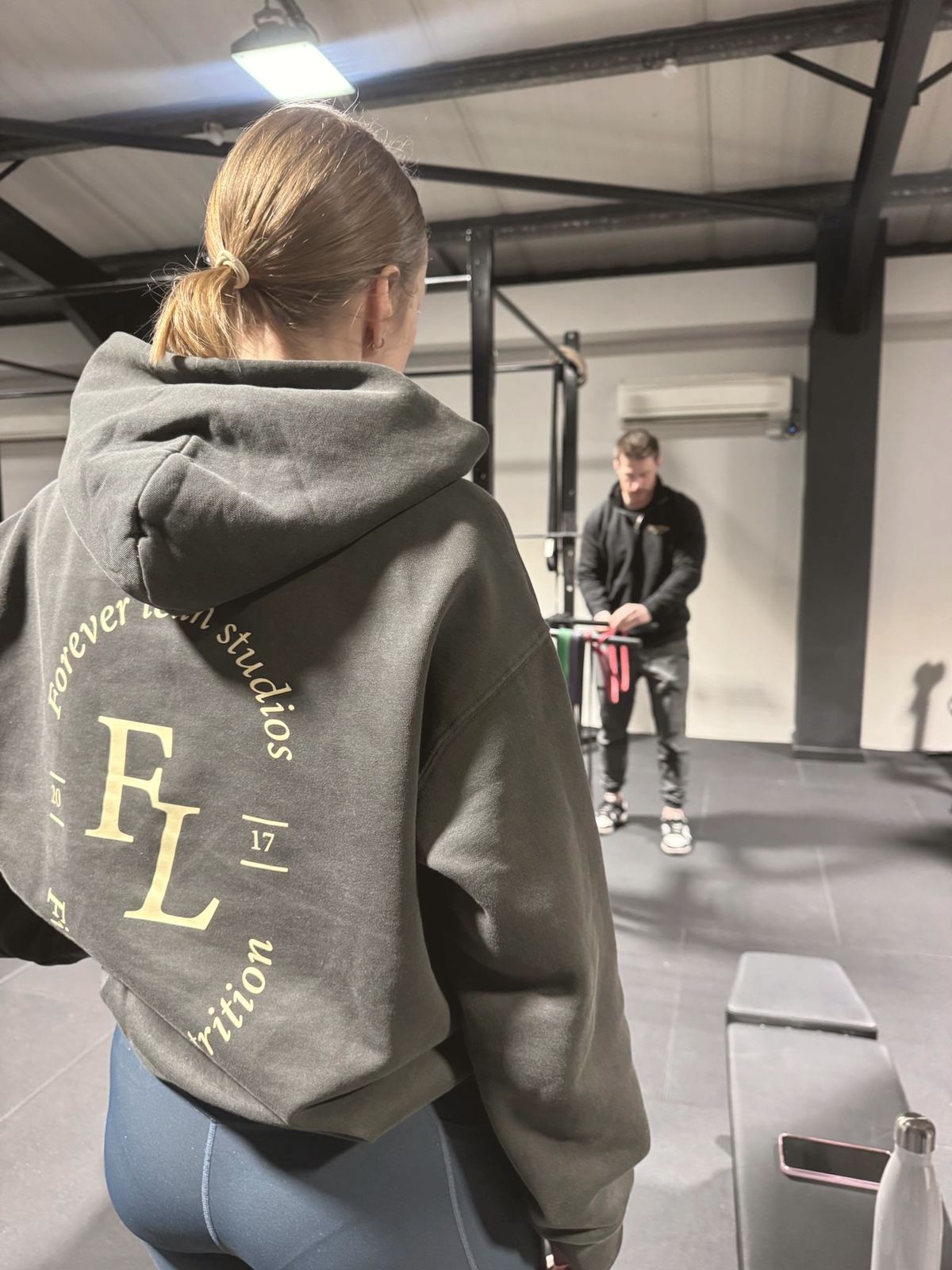 A member in a Forever Lean Studios hoodie, with a coach setting up behind her